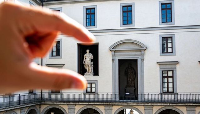 Pinching hand framing classical statues in museum facade, forced perspective architecture