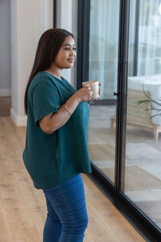 African american woman enjoying morning coffee by glass doors in contemporary home