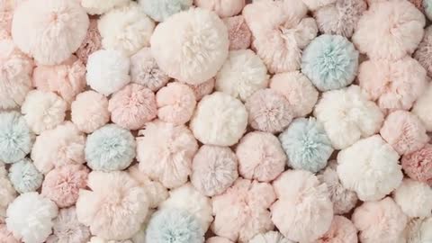 Camera panning across pastel yarn pom-poms showcasing fluffy texture and soft tufts