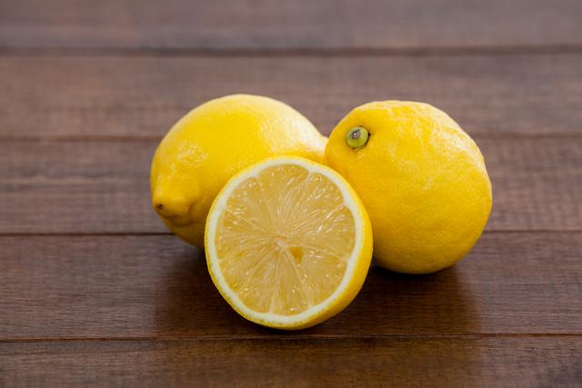 Close-up of fresh lemons on a wooden table, showcasing one whole lemon and one sliced in half. Ideal for use in food blogs, healthy eating articles, recipes, and advertisements for organic produce.