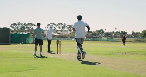 Cricketer running between wickets after hit with bowler on sunlit pitch