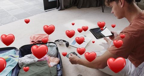 Young man packing suitcase and checking tablet and phone for travel planning at home