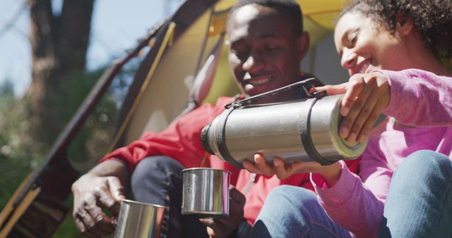 Couple enjoying tea while sitting in tent, signifying relaxation and enjoyment in nature. Perfect for use in topics related to camping, outdoor activities, couple bonding, leisure travel, and healthy lifestyles.