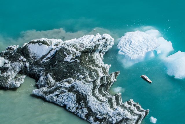 The image shows a small boat near an alien-like ice formation in clear blue glacial waters. Perfect for use in travel brochures, adventure and exploration magazines, promotional material for nature trips, or environmental awareness campaigns.