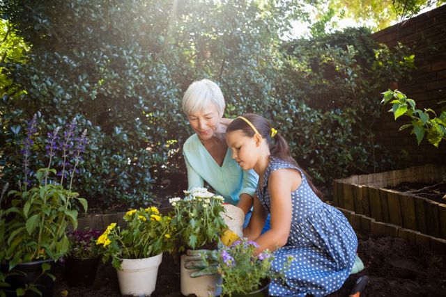 Grandmother looking at granddaughter planting flower pots in backyard