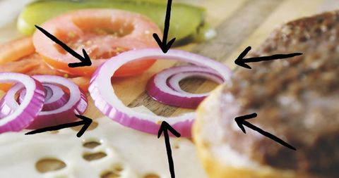 Closeup purple onion ring on swiss cheese with burger patty, tomato, pickle, black arrows