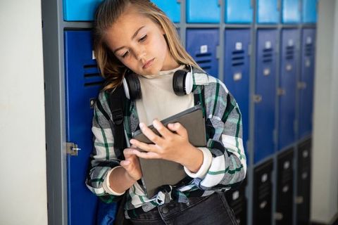 Preteen girl using tablet leaning on school lockers