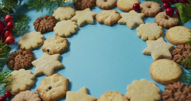 Festive assortment of Christmas cookies forming a frame on a blue background, decorated with pine branches and red berries. Ideal for holiday-themed advertisements, Christmas cards, social media posts, or baking websites. Conveys a warm, cheerful holiday atmosphere.