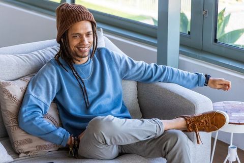 Relaxed young man with dreadlocks lounging on sofa in bright modern living room interior