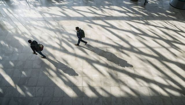 Diagonal shadow lattice over marble atrium with two walking pedestrians and backpacks