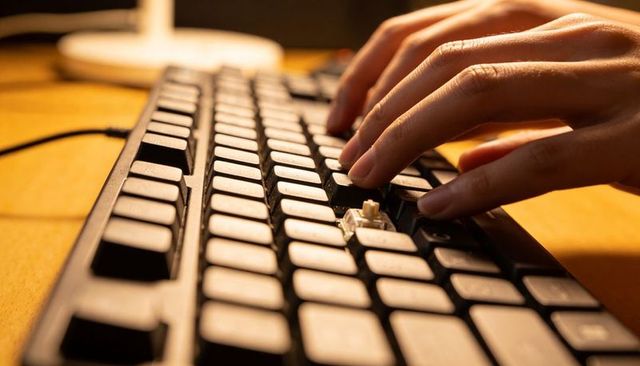 Hands typing on mechanical keyboard with exposed switch and removed keycap under warm lamp glow