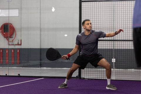 Male athlete playing padel on purple court preparing backhand with wide athletic stance