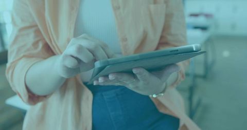 Young woman tapping tablet at classroom desk wearing orange shirt and white ribbed top