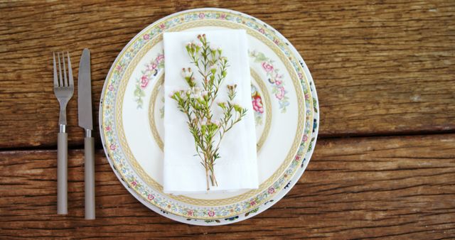 A vintage plate with floral patterns is set on a wooden table, accompanied by a fork and a napkin adorned with fresh greenery, with copy space. The arrangement suggests a rustic or country-style dining theme, emphasizing simplicity and natural elements.
