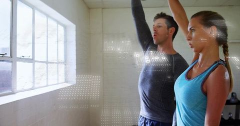Personal trainer coaching female client raising kettlebell in bright window-lit studio