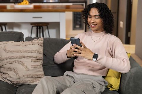 Young asian man relaxing on sofa using smartphone and smartwatch in modern apartment