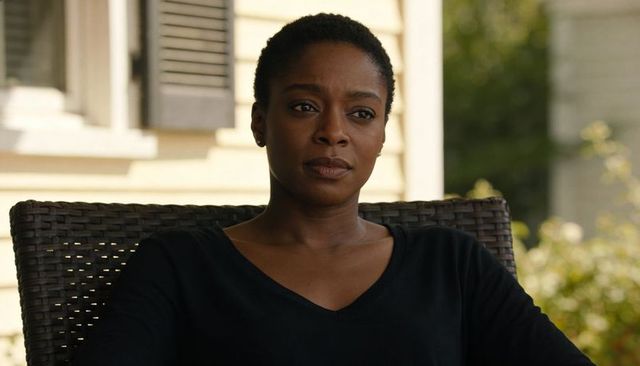 Woman sitting on porch wearing black v-neck top looking thoughtful in warm sunlight