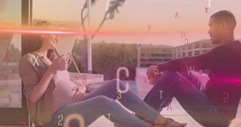 Expecting couple chatting and relaxing on sunset patio holding mugs and touching belly