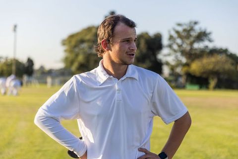 Young cricketer standing on sunlit field watching play wearing white kit and wristwatch