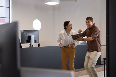 Diverse professionals celebrating success with technology in modern office