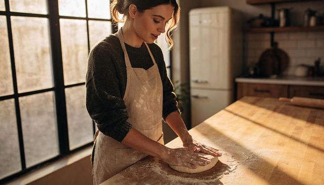 Sunlit artisan baker kneading dough on rustic wooden island in warm morning light