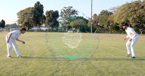 Cricket fielders crouching and practicing with teal holographic orb on grassy park
