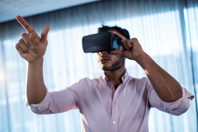 Businessman using virtual reality headset in office, interacting with virtual environment. Ideal for illustrating modern technology in business, innovation in the workplace, and professional use of VR for presentations or training.