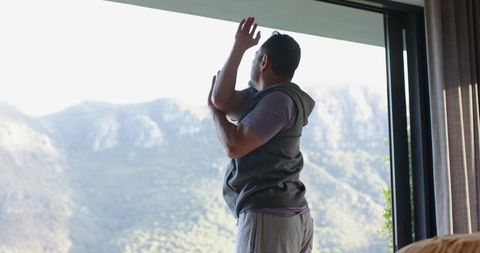 Man Stretching by Window Overlooking Mountain View in Casual Attire