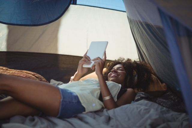 Young woman using digital tablet while lying down in tent at campsite