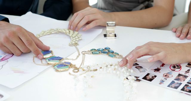 Designers selecting and discussing various intricate necklace designs at jewelry workshop. Involves explorations of sketches and samples with attention to detail for creative decision-making. Perfect for depicting jewelry design processes, craftsmanship, creative workplace.