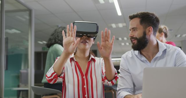 Woman enthusiastically wearing and exploring with a virtual reality headset while interacting with colleagues in a modern office environment. Ideal for themes such as workplace technology integration, team collaboration, innovation, and modern work culture.