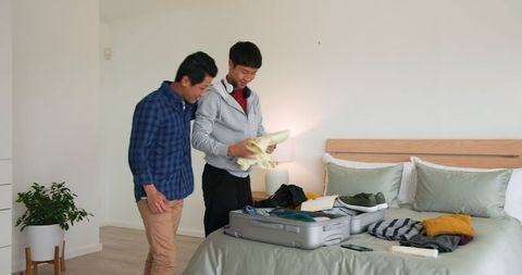 Friends packing suitcase together in cozy bedroom for travel