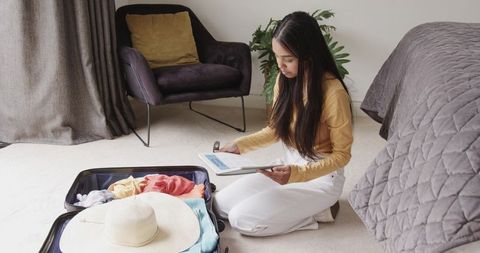 Asian woman packing suitcase and checking luggage weight with digital scale at home