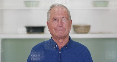 Senior man smiling at home wearing blue button-down shirt relaxed in modern kitchen