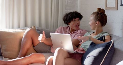 Diverse couple engaging on sofa with laptop in bright living room