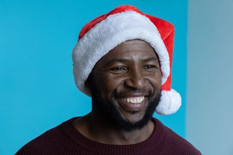 Smiling african american man wearing santa hat and maroon sweater on cyan background