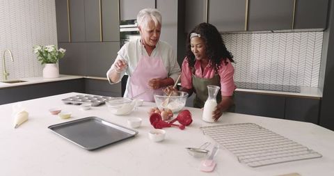 Senior woman and african american woman baking muffins together in modern kitchen