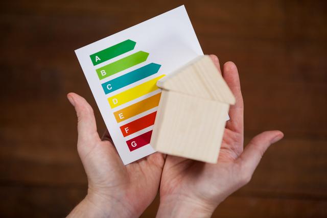 Woman holding miniature house with energy efficiency rating chart