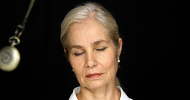 Mature woman with eyes closed under hypnosis, appearing calm and relaxed. Ideal for use in articles or advertisements related to hypnosis therapy, mental health, stress relief, relaxation techniques, or wellness programs.