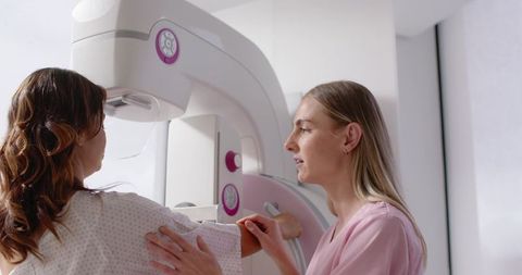 Female technologist positioning patient during mammogram screening in clinical radiology
