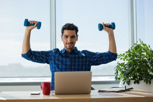This image depicts a smiling executive multitasking by exercising with dumbbells while working on a laptop at his office desk. Ideal for articles or advertisements focusing on workplace wellness, productivity, and the importance of maintaining a healthy lifestyle even during work hours. Can be used in blogs, corporate wellness programs, fitness promotions, and business-related content.
