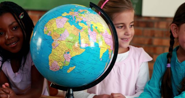 Cute pupils smiling around a globe in classroom in elementary school