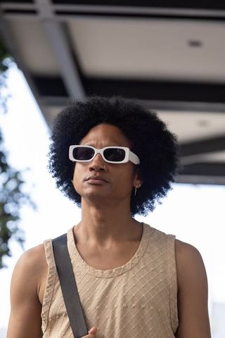 Urban african man standing beneath canopy wearing white rectangular shades and beige sleeveless top
