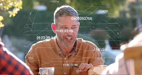 Mature man leaning forward during garden patio meal, laughing, talking and sharing bread