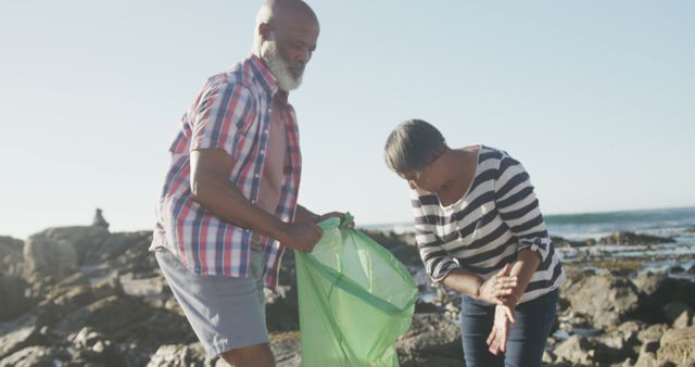 Diverse senior couple collecting rubbish for recycling on sunny beach. Retirement, ecology, summer, vacations, volunteering and senior lifestyle, unaltered.