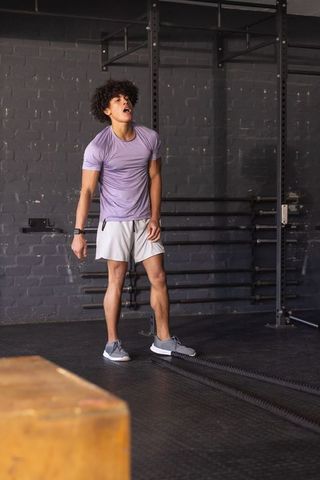 Young african american man catching breath after battle rope workout in gym with plyo box