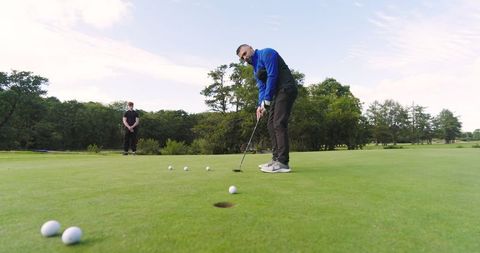 Father Teaching Teenage Son Golf Putting Technique on Green