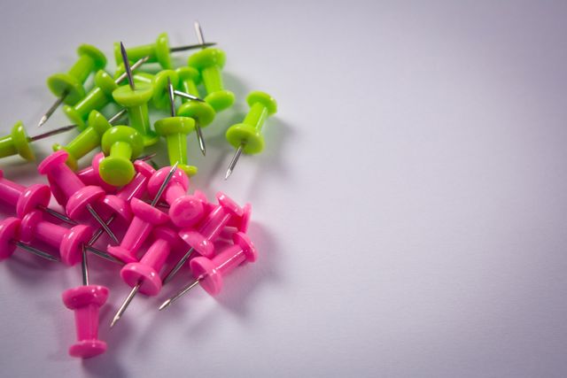 This image shows a close-up view of green and pink push pins scattered on a white background. Ideal for use in articles or advertisements related to office supplies, organization tips, school supplies, or colorful stationery. It can also be used in educational materials or blogs discussing office or school organization.