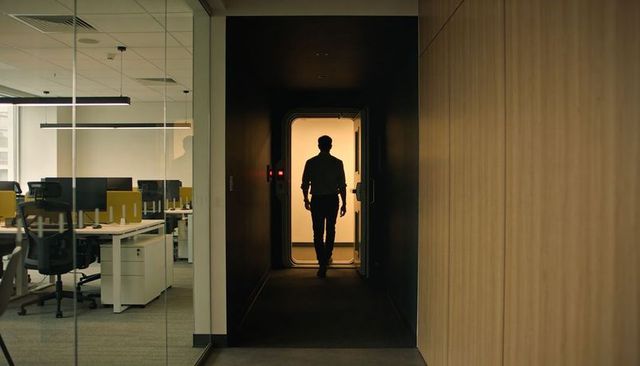 Silhouetted professional walking toward warm-lit doorway in modern open-plan office