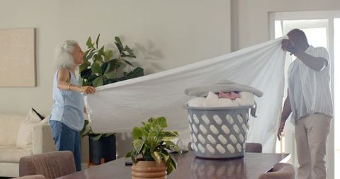 Diverse couple folding laundry together in modern home